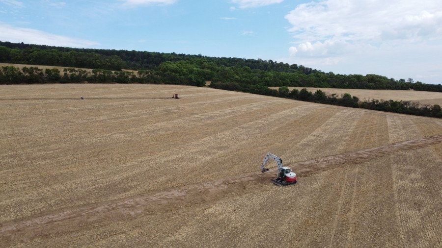 Auf einem Feld wird über einen Bagger ein Graben ausgehoben