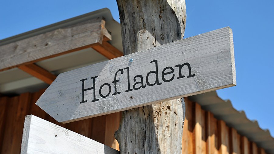 An einem Pfahl wurde ein wegweisendes Schild mit der Beschriftung „Hofladen“ angebracht. 