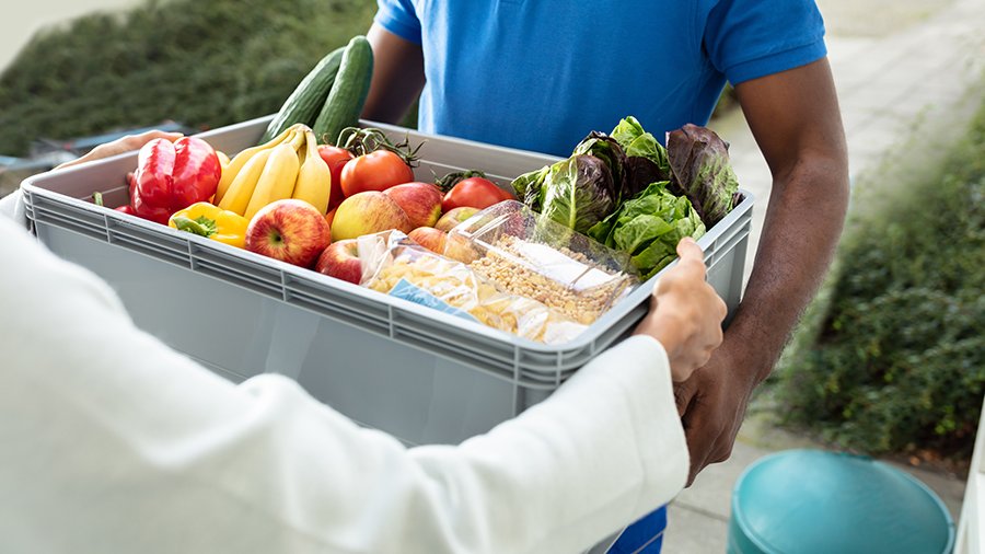 Lieferant übergibt Kiste mit Obst und Gemüse an Kundin.