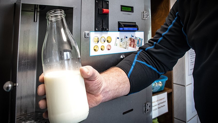 An einem silbernen Milchautomaten wird eine Glasflasche mit Milch befüllt.