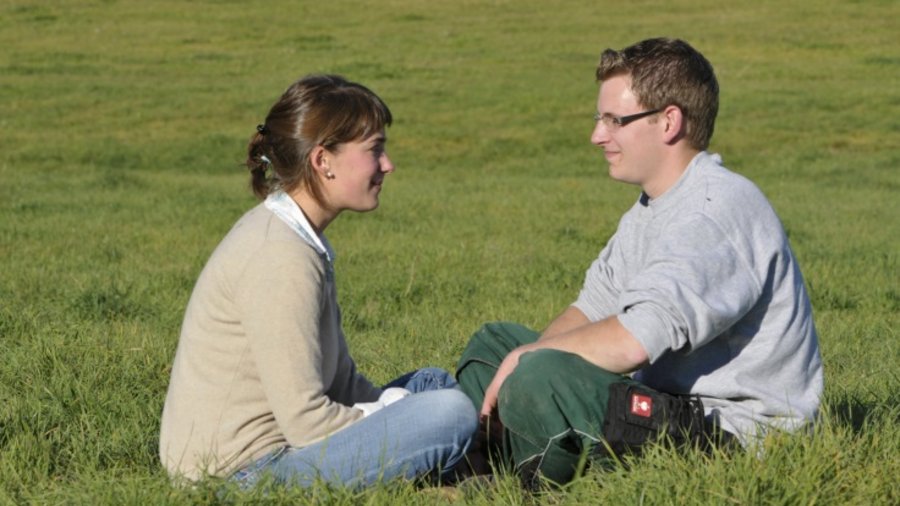 Junges Paar sitzt sich auf der Weide gegenüber und schaut sich gegenseitig an.